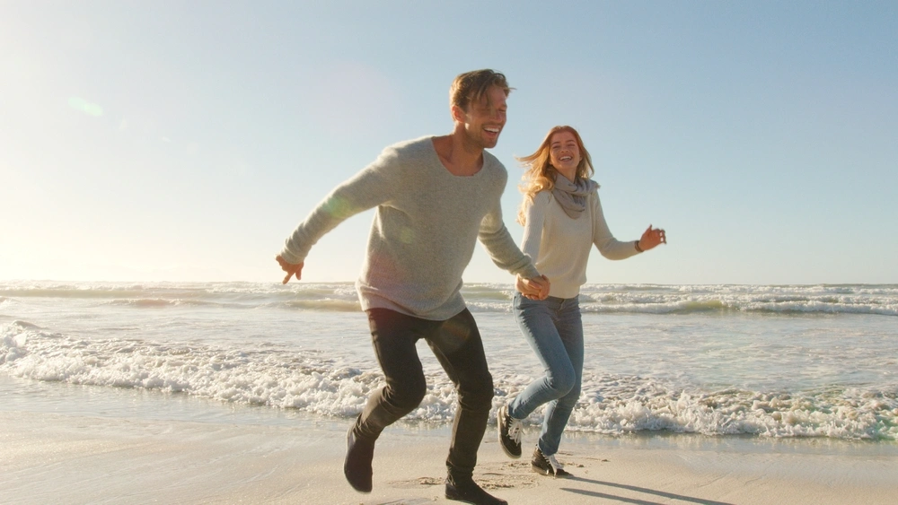 Two people smiling while running on the beach